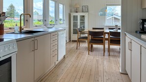 A kitchen with white cabinetry, a wooden dining table with chairs, and a view of the outdoors through large windows. - 3 bedroom stunning home in øster assels (Øster Assels)