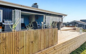 Ein modernes Haus mit Holzterrasse, Sitzgelegenheit im Freien und Grill.