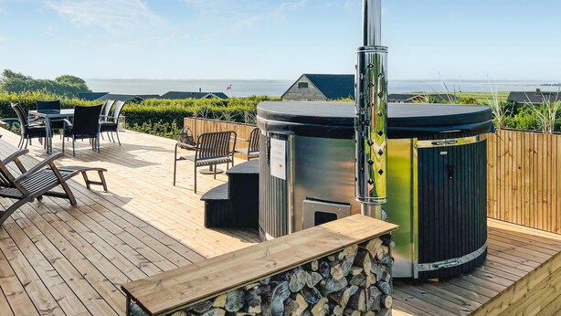 A wooden deck with outdoor furniture, a hot tub, and a view of the sea. - 3 bedroom stunning home in øster assels (Øster Assels)