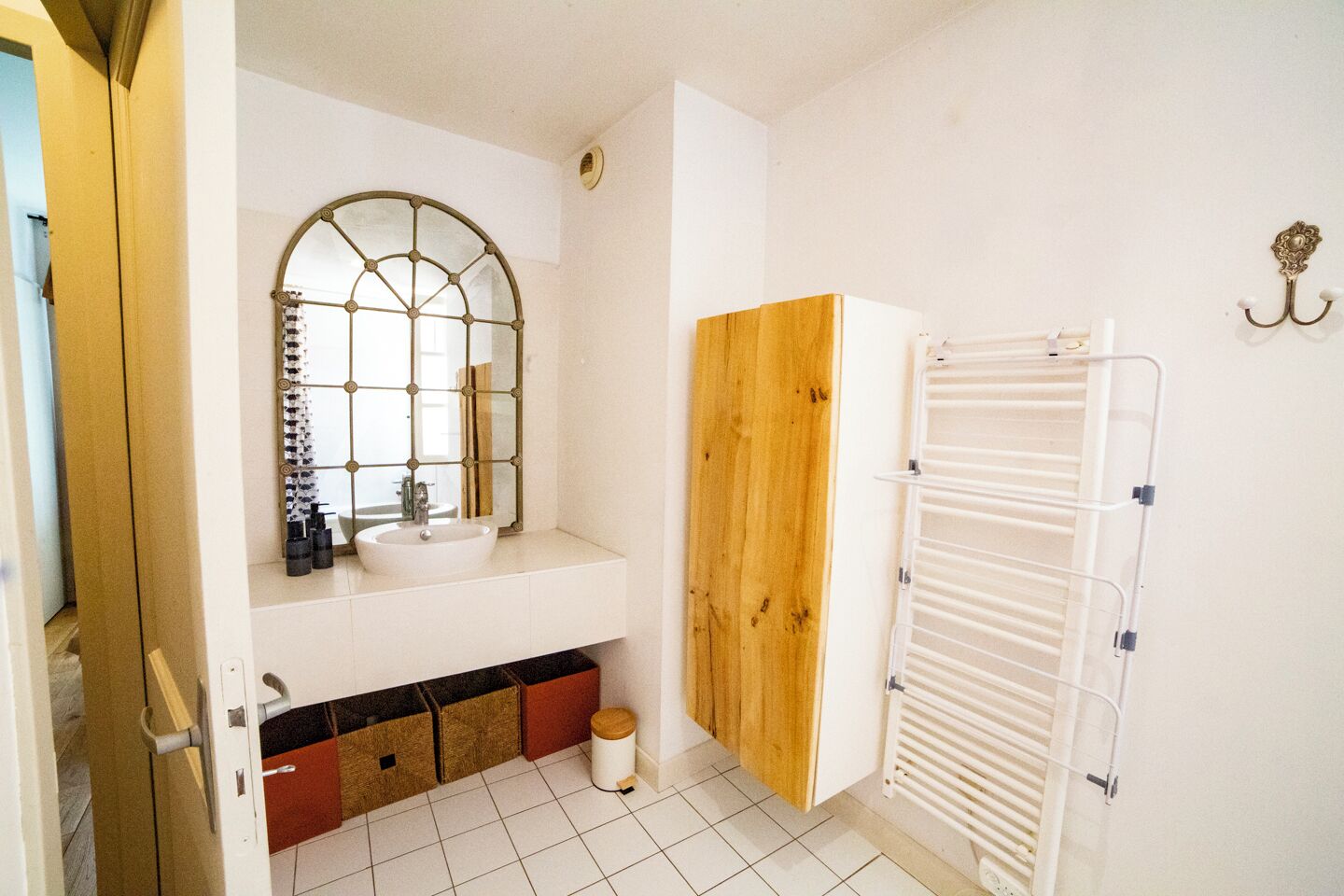 Un bagno con lavandino bianco, uno specchio con cornice decorativa, una porta in legno e un portascopevoli bianco.