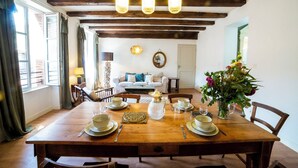 A dining room with a wooden table set for four, a chandelier, and a view of the living area with a sofa and a mirror.