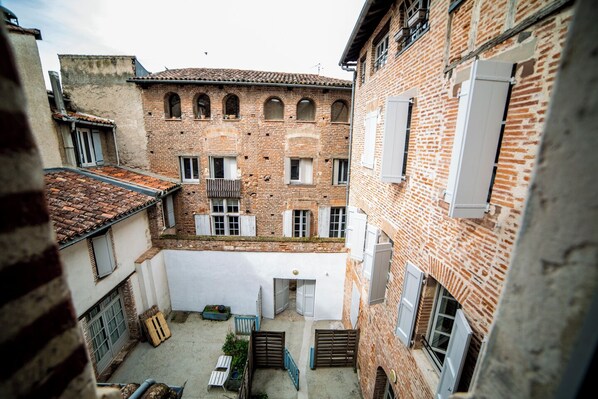 Un patio con un edificio de ladrillo, una pared blanca y un pequeño jardín.