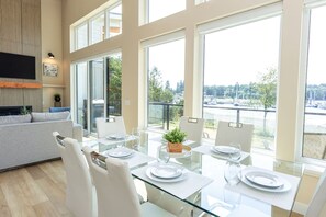 A modern dining area with a glass table, white chairs, and a view of a body of water.