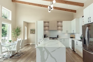A modern kitchen with a marble island, wooden beams, and white cabinetry.