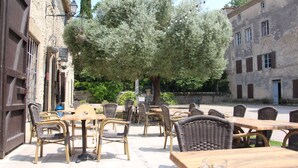 Un patio al aire libre con mobiliario de mimbre, un edificio de piedra y un árbol.