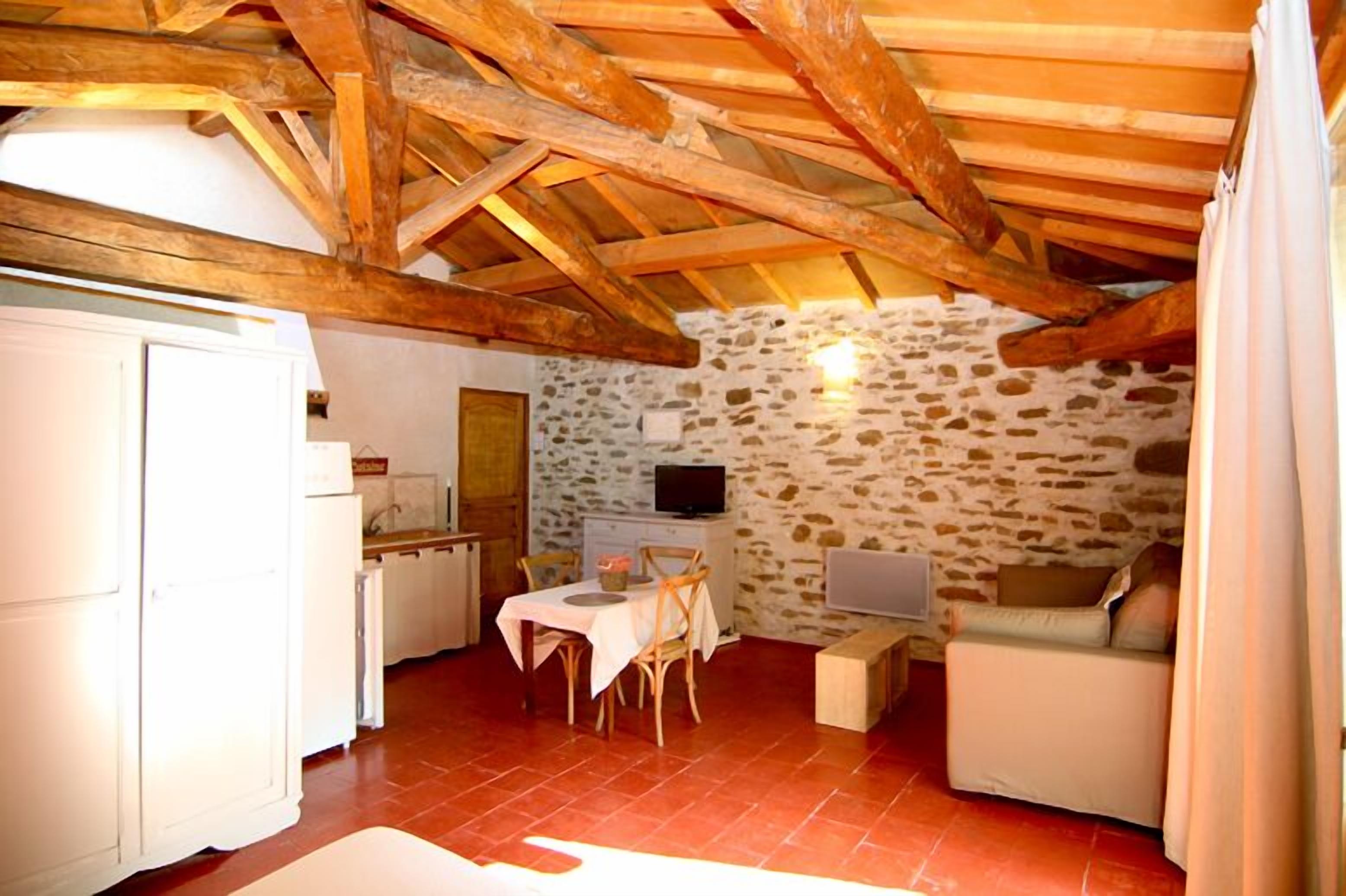 A rustic room with exposed wooden beams, a stone wall, a dining table with chairs, a sofa, and a television.