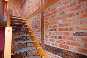 Un escalier en colimaçon en bois, avec des marches recouvertes de moquette, adossé à un mur de briques.