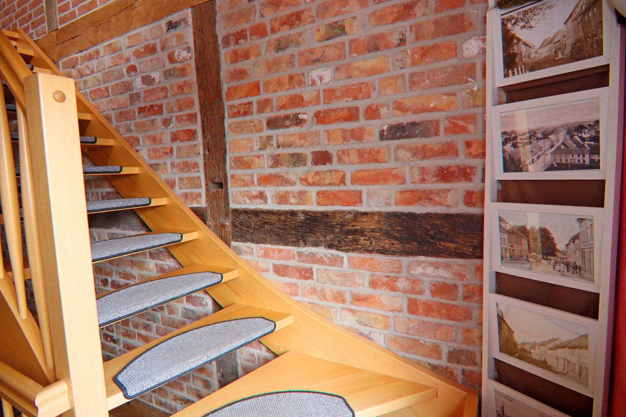 A wooden spiral staircase with a brick wall background and framed pictures on the right.