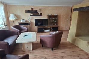 A furnished living room with a sofa, armchair, TV, and a cabinet with glassware.