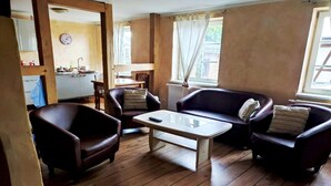 A cozy living room with wooden flooring, a glass coffee table, and two leather armchairs. A kitchen is visible in the background. - Ferienwohnung Kogge im Zentrum von Röbel (Röbel)