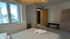 A bedroom with a bed, two towels, a bench, a wardrobe, and a window with a view of greenery. - Agreen Country House Juniper (Sardegna)