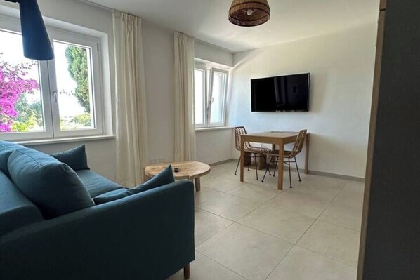 A modern living room with a blue sofa, a small round table, and a TV mounted on the wall.
