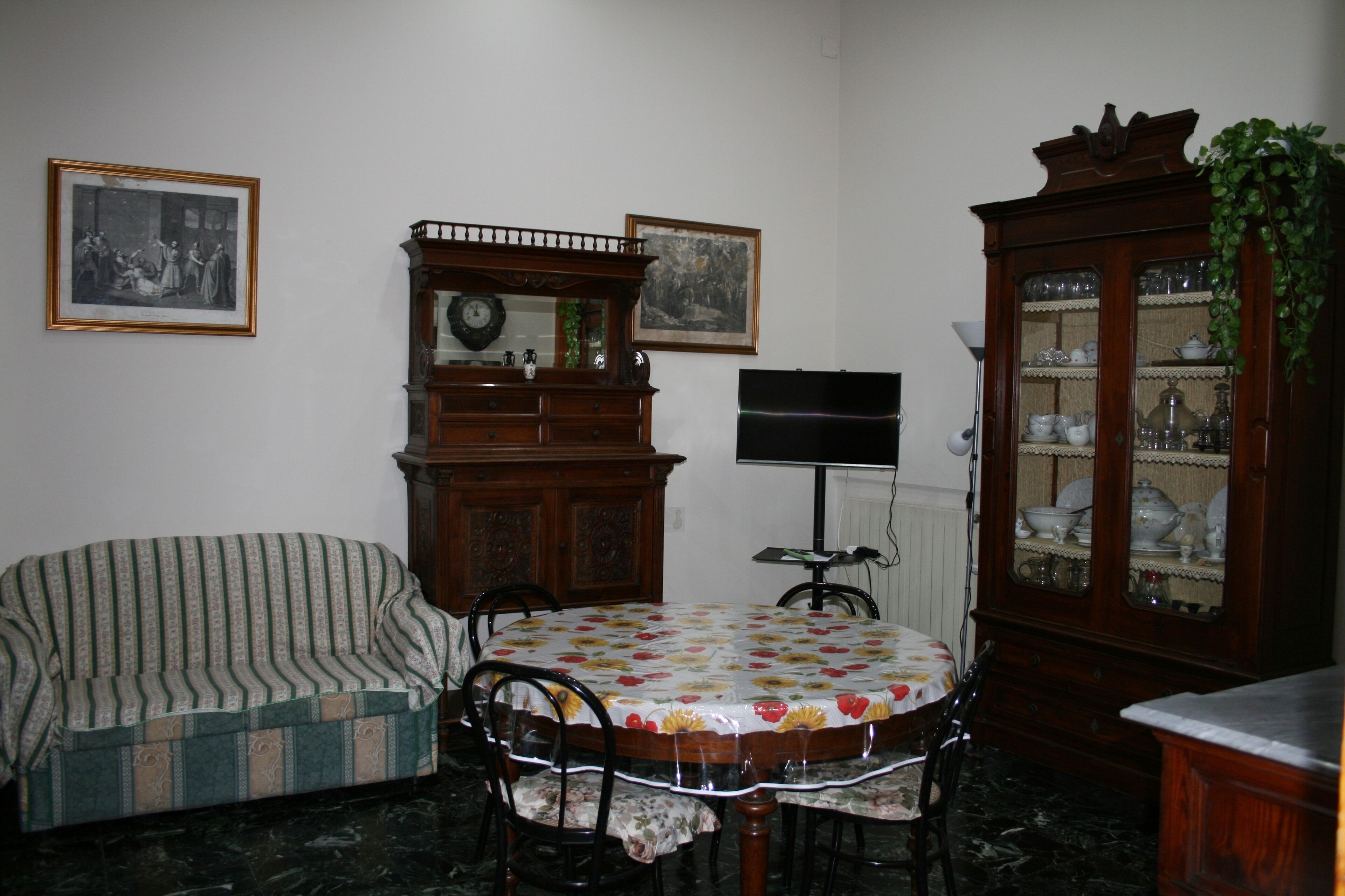 A dining area with a round table, chairs, a sofa, a wooden cabinet, and framed pictures on the wall.