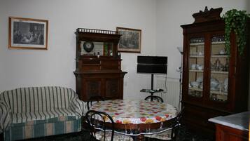 A dining area with a round table, chairs, a sofa, a wooden cabinet, and framed pictures on the wall.