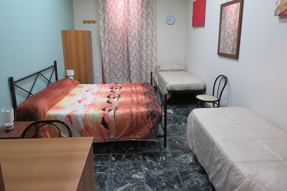Una habitación pequeña y funcional con cama, una silla, una mesa y un espejo en la pared.