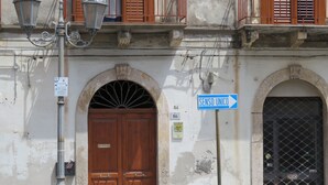 A building with a large wooden door, a street sign, and a metal gate. - Sole&Luna (Milazzo)