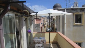 A small balcony with a table and chair, a white umbrella, and a view of the cityscape. - Sole&Luna (Milazzo)