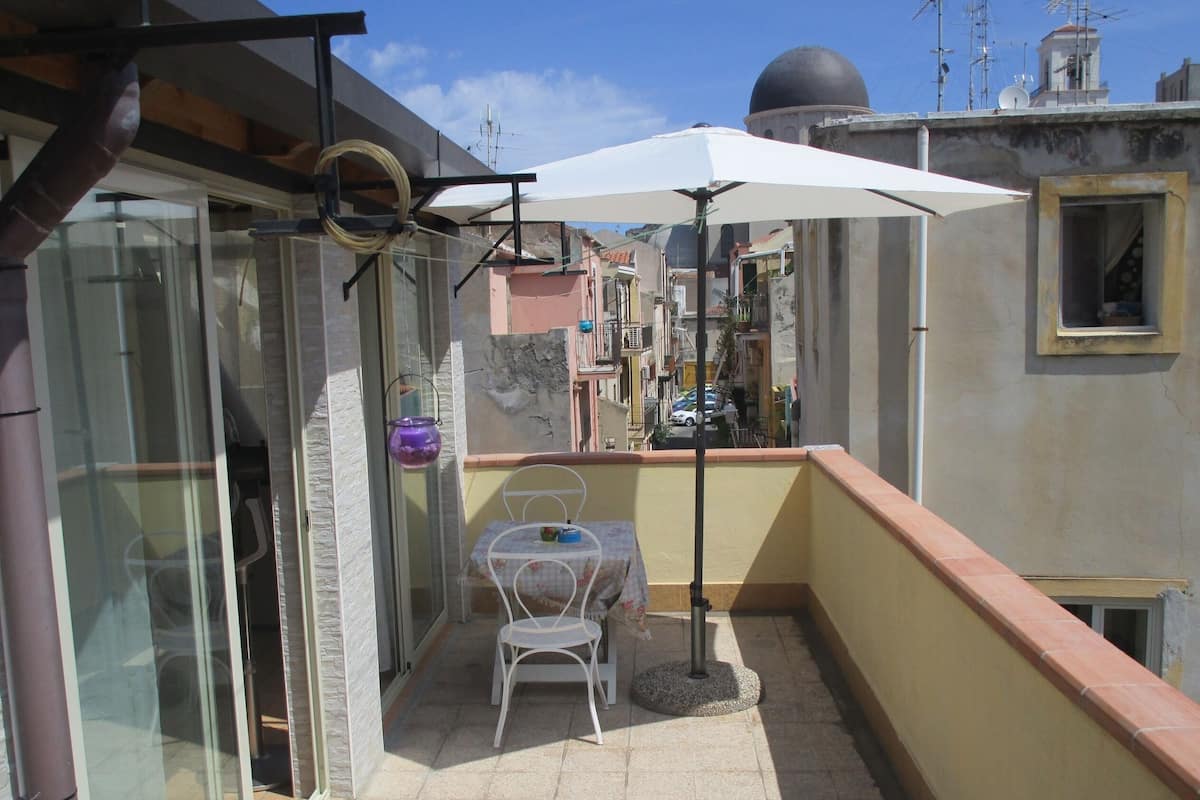 Un pequeño balcón con una mesa, una silla y una sombrilla blanca, con vista a la ciudad.