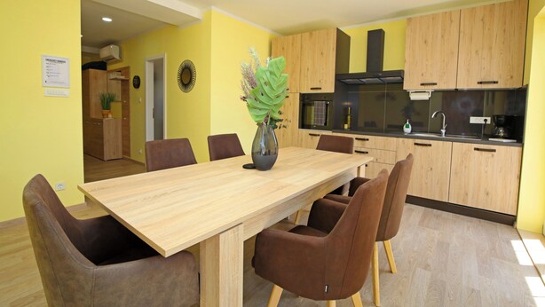Una cocina moderna con armarios de madera, encimera negra y un comedor con mesa de madera y sillas marrones.