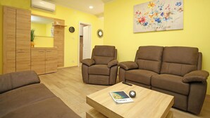 Una sala de estar con dos sofás marrones, una mesa de centro de madera con un libro y un control remoto, y un cuadro floral en la pared.