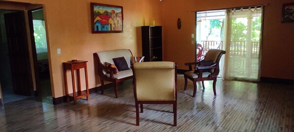 A living room with wooden flooring, a sofa, two armchairs, a small table, and a painting on the wall.