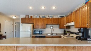 A kitchen with wooden cabinets, a refrigerator, a microwave, a sink, a stove, and a coffee maker. - Reel Relaxin - Waterfront Pool, Indoor Pool & Hot Tub! (Village of Four Seasons)