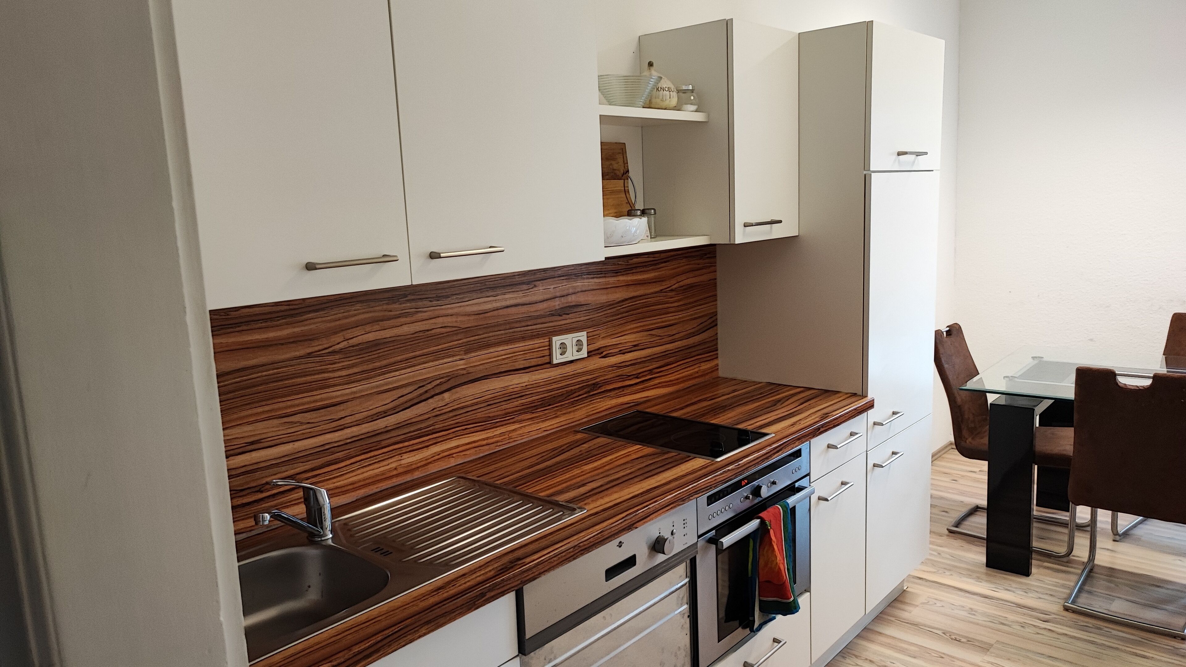 Eine moderne Küche mit Holzarbeitsplatten, einem eingebauten Ofen und einem Essbereich mit einem Glastisch und Stühlen.