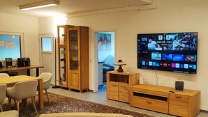 A modern living room with a flat-screen TV, wooden furniture, and a dining area. - Gesamtes großen Haus bis 21 Personen (Veitshöchheim)