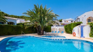 A swimming pool with blue tiles, surrounded by palm trees and white buildings.
