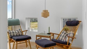Ein Zimmer mit zwei Holzsesseln mit Kissen, einem kleinen Tisch mit Kerze und einer hängenden Deckenleuchte.