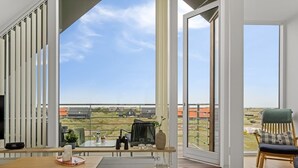Ein geräumiges Wohnzimmer mit einem großen Schiebeglasfenster, das auf einen Balkon führt. Das Zimmer verfügt über Holzdielen, ein Sofa, einen Couchtisch und einen Fernseher.