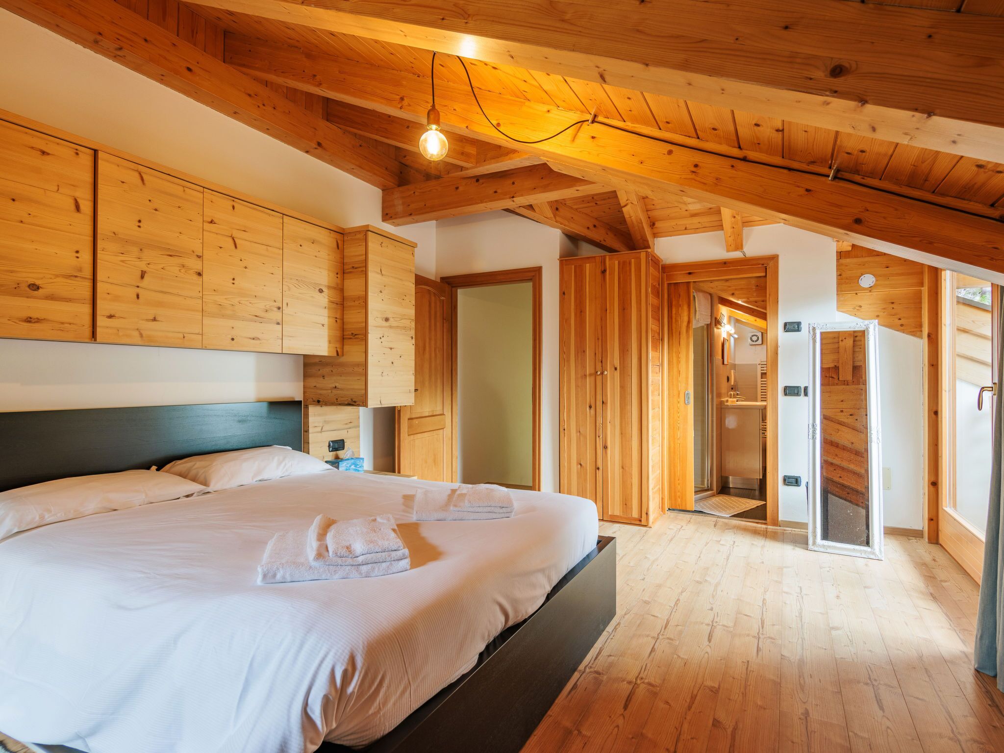 Ein Schlafzimmer mit Holzboden, einem großen Bett und einem durchgehenden Türrahmen sichtbaren Badezimmer.