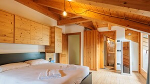 Een slaapkamer met een houten plafond, een groot bed en een badkamer zichtbaar door een geopende deur.