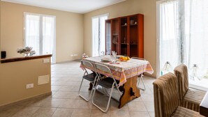 Un coin repas avec une table dressée pour deux personnes, un buffet contenant de la verrerie, et une vue sur l’extérieur grâce à de grandes fenêtres.