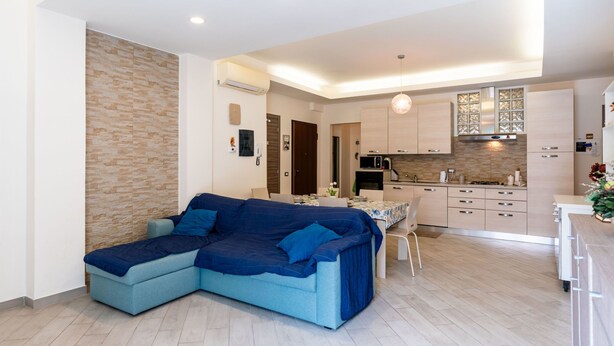 A modern living room with a sectional sofa, a dining table, and a kitchen area with cabinets and a microwave. - La dimora del pontile by Interhome (Ceriale)