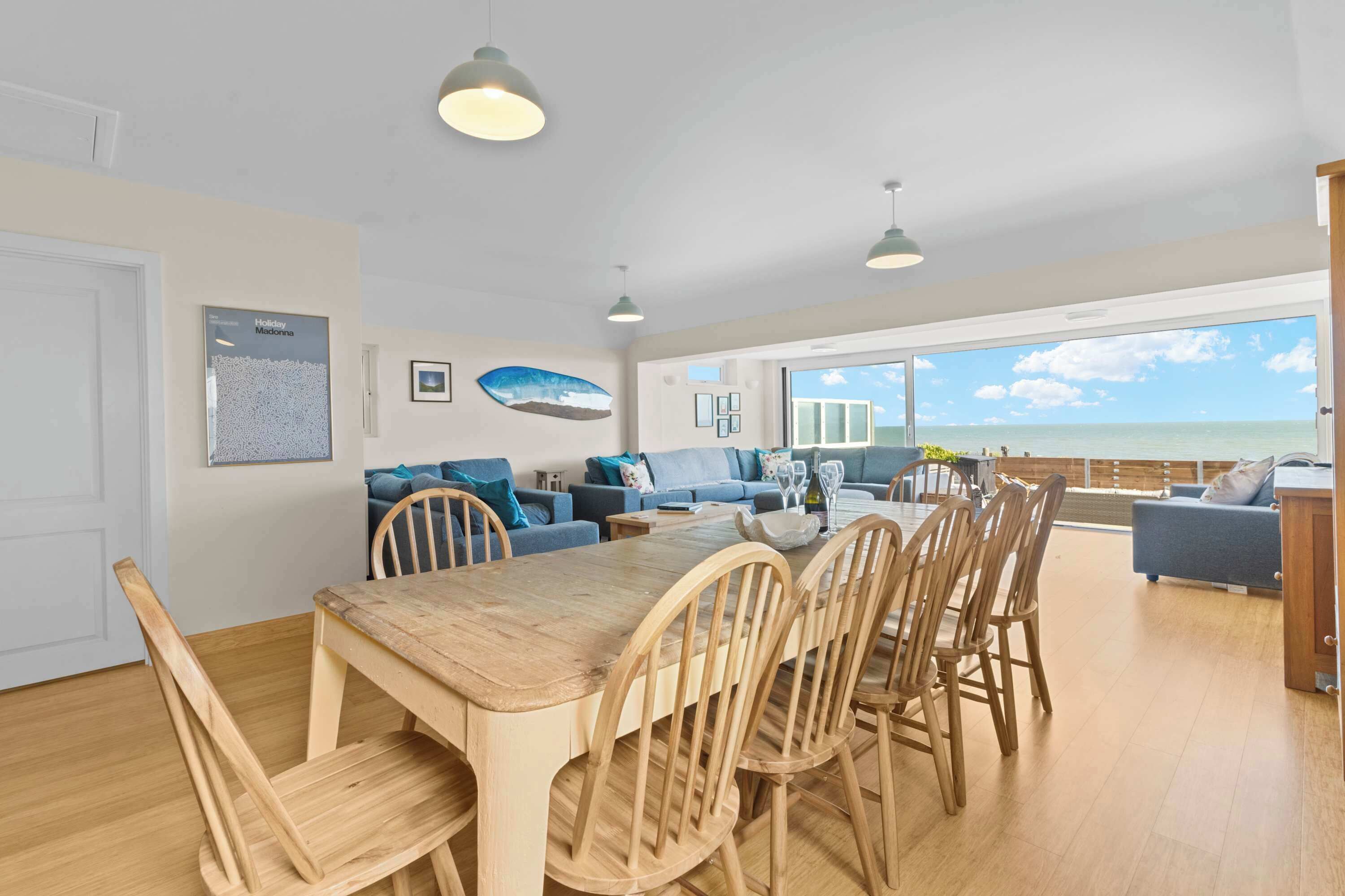 Un vaste espace de vie comprenant une table et des chaises en bois pour la salle à manger, un ensemble de canapés et une grande fenêtre donnant sur la mer.
