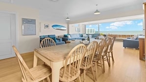 Un amplio salón con una mesa y sillas de madera, un conjunto de sofá y un gran ventanal con vistas al mar.