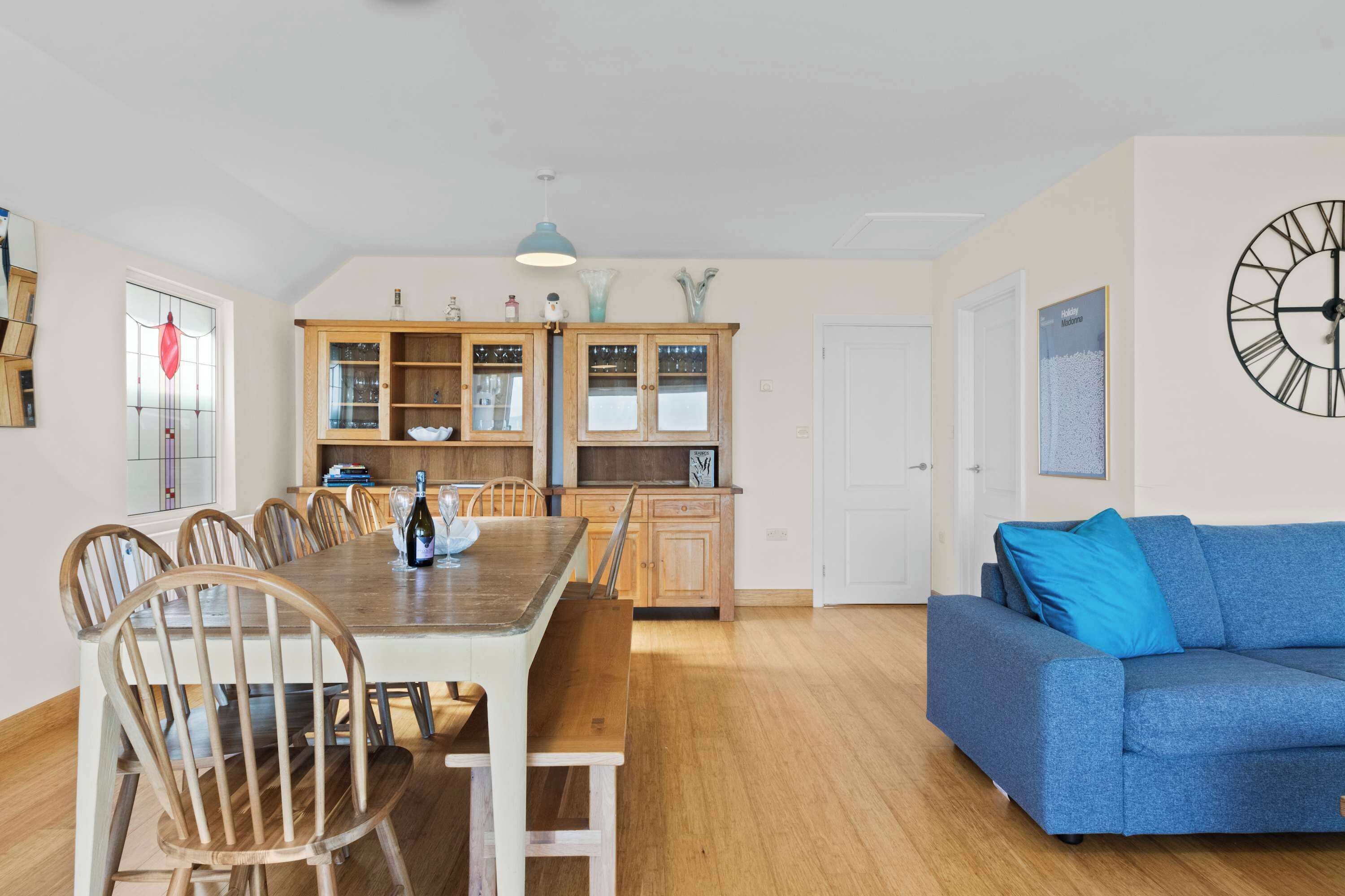 Un salón espacioso con una mesa de comedor de madera, un sofá azul y un reloj de pared grande.
