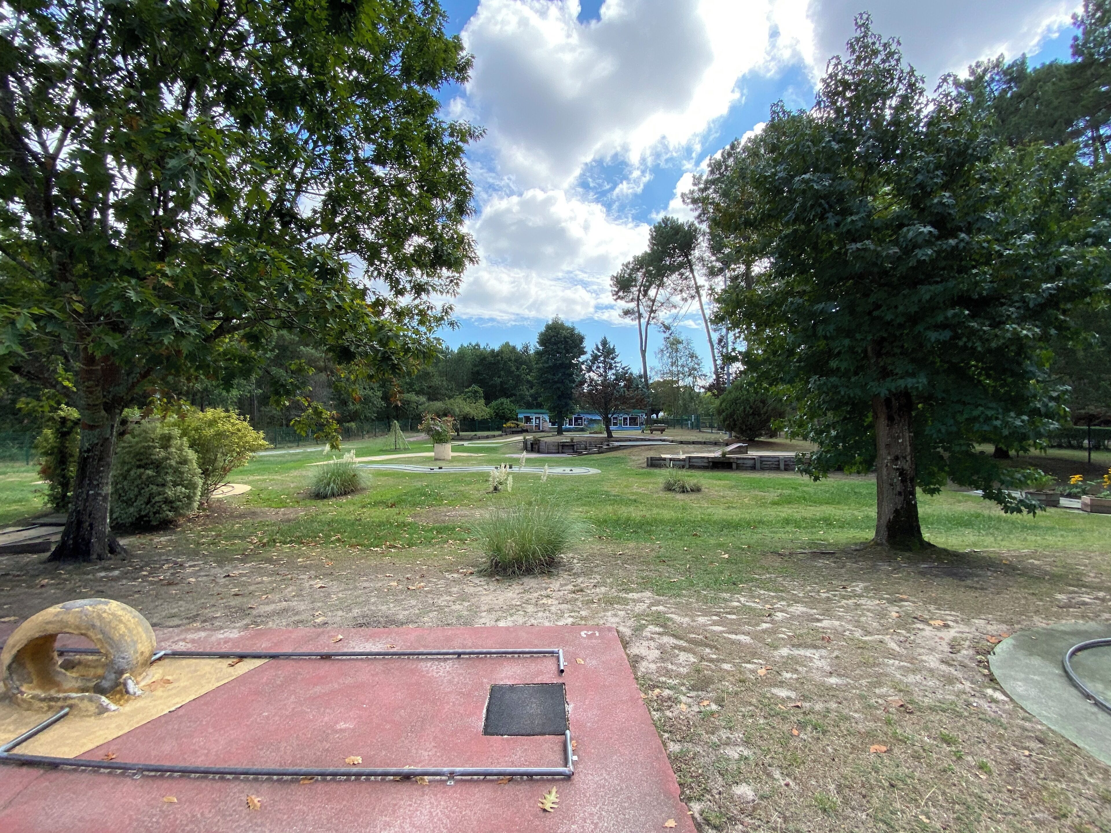 A park with a red play area, green grass, and trees.