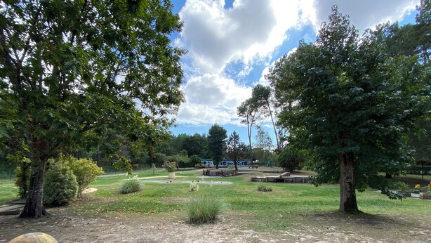 Ein Park mit einem roten Spielbereich, grünem Rasen und Bäumen.