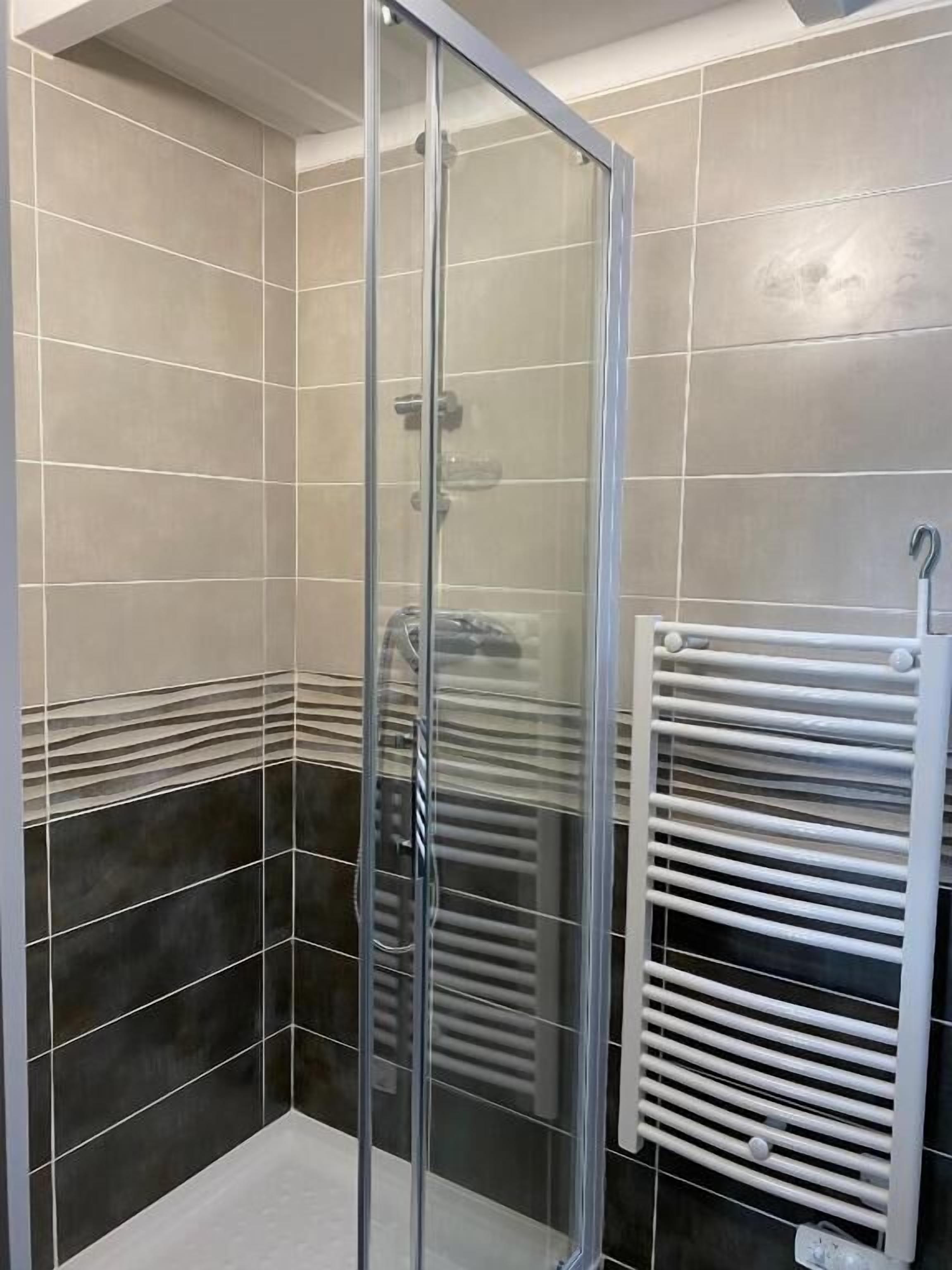 A glass-enclosed shower with a white towel rack beside it.