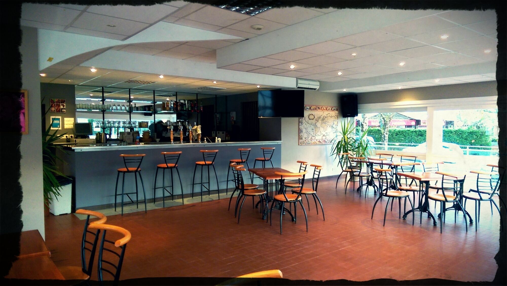 A restaurant with a bar area, multiple tables and chairs, and a view of the outdoors.