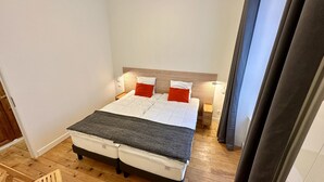 Ein kleines, ordentlich eingerichtetes Schlafzimmer mit einem Einzelbett, einem Nachttisch und einer Lampe.