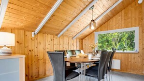 A cozy wooden room with a dining table, chairs, a lamp, and a window with a view of greenery.