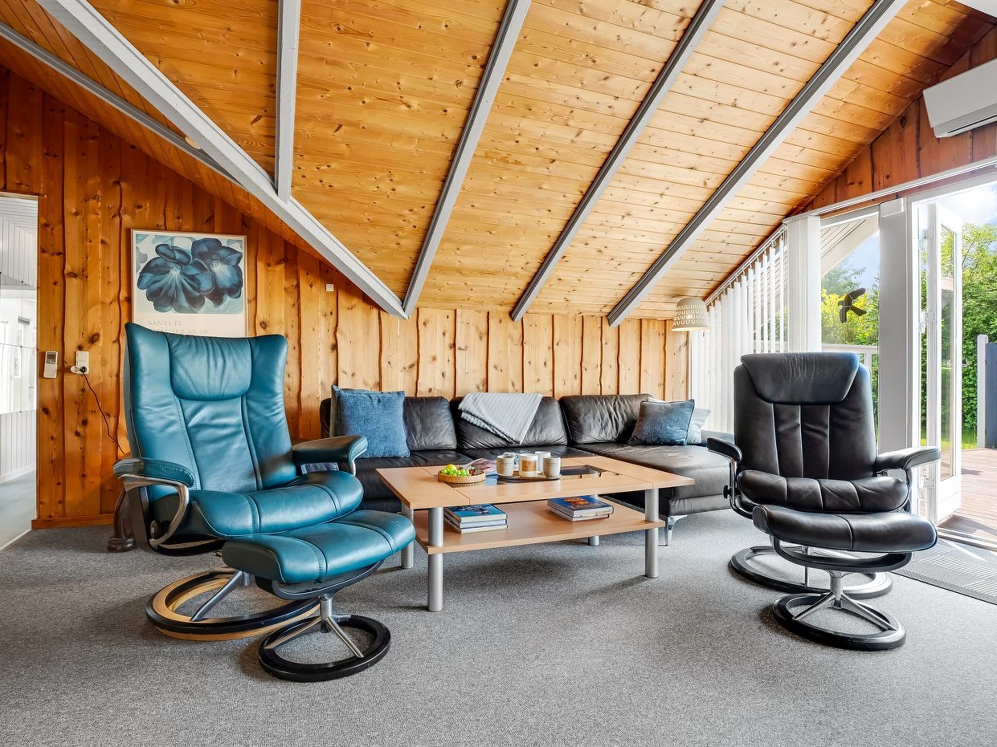 Een gezellige woonkamer met een houten plafond, een bank, twee leren fauteuils en een salontafel met boeken en een fruitschaal.