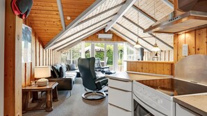 A cozy cabin interior with a dining area, a kitchen with a stove, and a large window offering a view of the outdoors.