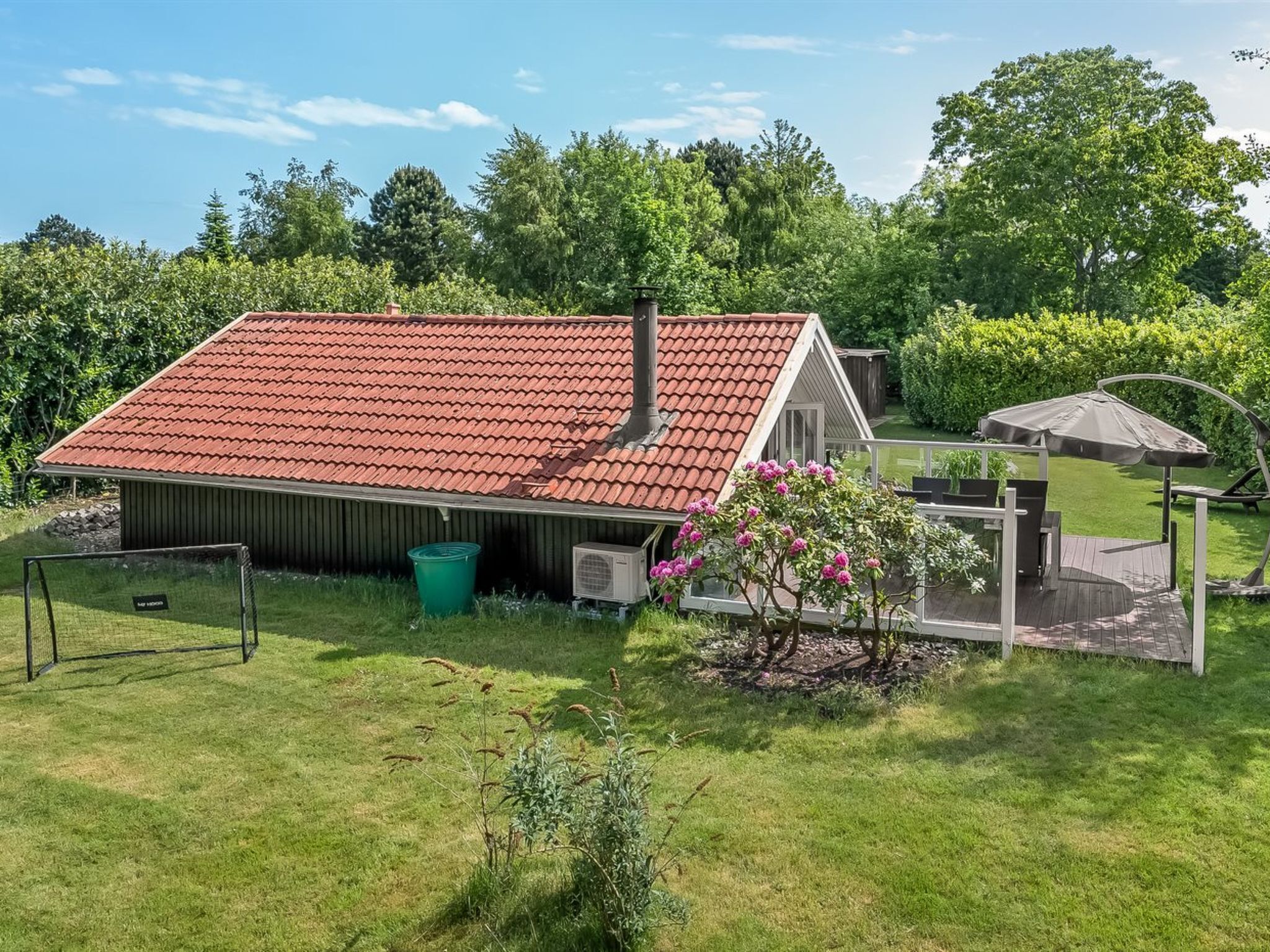A house with a red tiled roof, a small porch, and a garden with a pink flowering plant.