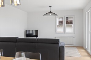 A modern living room with a sofa, a TV, a pendant light, and a window with a view of a balcony. - Beautifully renovated apartment with a view, in Savièse (Saint-Germain (Savièse)
