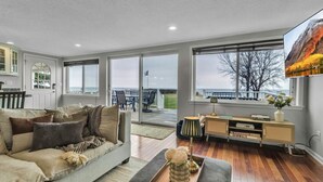A spacious living room with a large window, a sofa, a coffee table, and a sideboard. - Lakefront 5 Bds, sleeps 8 -Blue Waters Cottage (Ransomville)