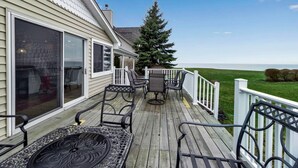 A wooden deck with outdoor furniture, a white railing, and a view of the ocean. - Lakefront 5 Bds, sleeps 8 -Blue Waters Cottage (Ransomville)